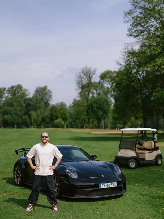Milestone portrait beside a dark sports car